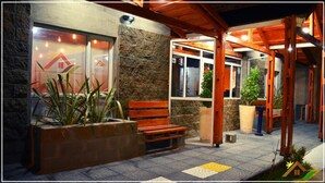 A covered outdoor area with a bench, potted plants, and a building entrance with glass doors. - Meraki Hotel (Las Heras)