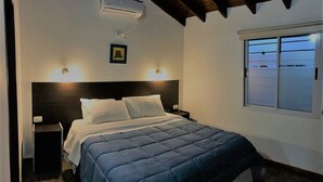 A bedroom with a bed, nightstands, an air conditioner, a framed picture, and a window with a view. - Hosteria el Puente (Merlo)
