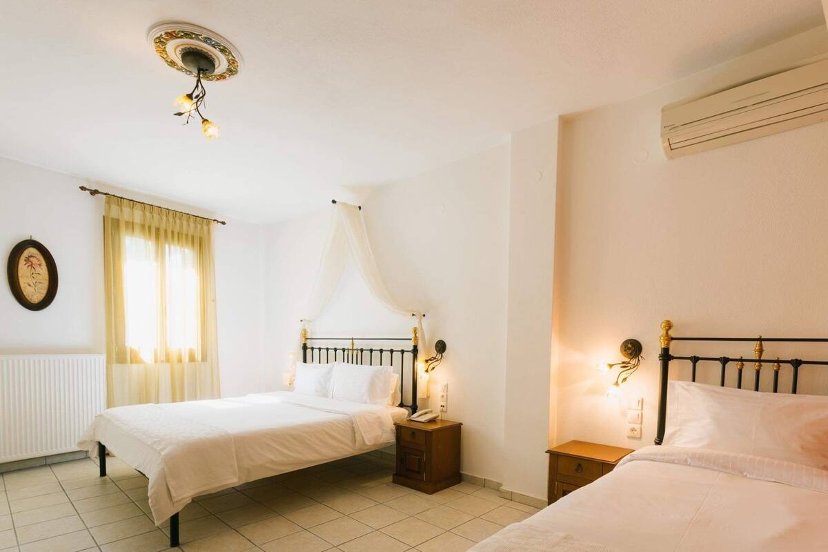 Quarto duplo com cama de dossel, mesas de cabeceira com luminárias, radiador e relógio fixado na parede.