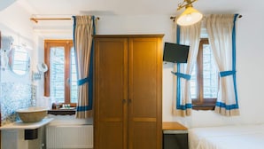 A bedroom with a wooden wardrobe, a bed, a small table, a radiator, and a window with curtains.