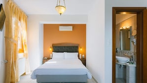 A hotel room with a bed, bedside lamps, a nightstand, a bathroom with a sink and mirror, and a door leading to another room.