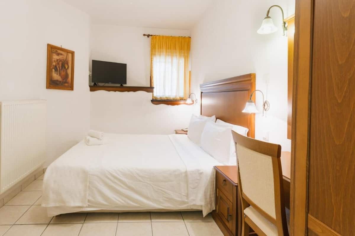 Quarto bem arrumado com uma cama, mesas de cabeceira, uma TV na parede e uma janela com cortinas.