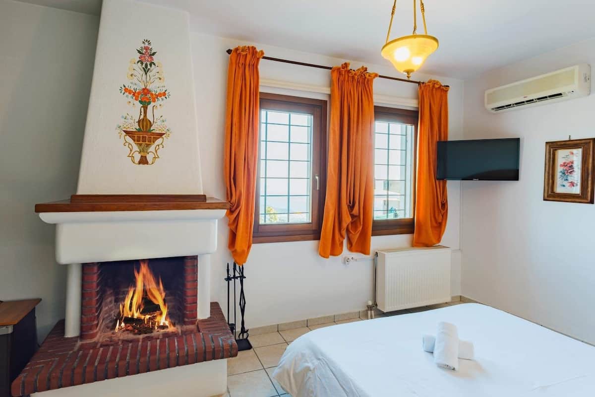 Quarto com lareira, cama, janela com cortinas, televisão e aparelho de ar condicionado.
