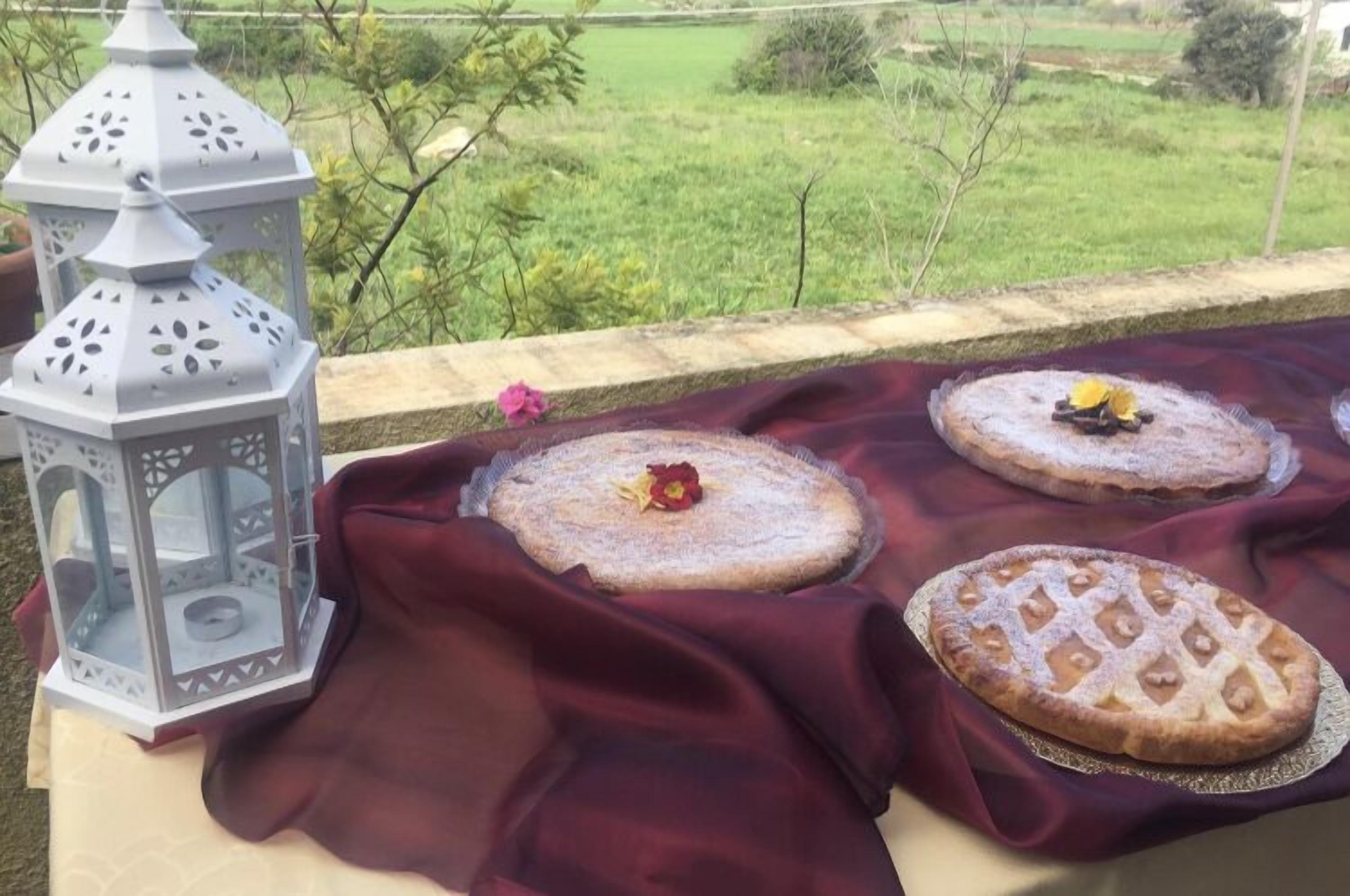 A table with three cakes on a red cloth, a white lantern, and a view of a green field.
