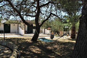 A courtyard with a hammock, a tree, and a building with a white facade and green shutters.