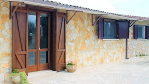 Eine Fassade aus Stein mit einer Holztür und Fenstern, einem Blumentopf und einem gepflasterten Eingangsbereich.