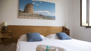 Ein ordentlich bezogenes Bett mit zwei Kissen, einem Kopfteil, Nachttischen inklusive Lampen und einem Gemälde eines Turms an der Wand.
