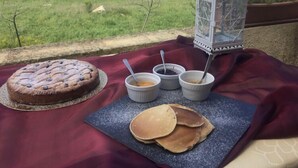 Ein Tisch mit Kuchen, Pfannkuchen und drei Sirup-Schalen, auf einem Balkon mit Blick auf ein grünes Feld.