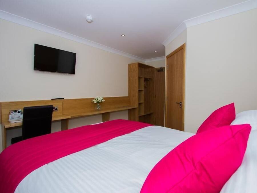Quarto de hotel com cama, escrivaninha, cadeira, televisão e guarda-roupa.