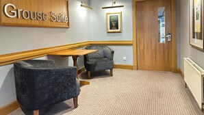 A hotel lobby with a 'Grouse Suite' sign, two armchairs, a wooden table, and a framed picture on the wall. - Hill Park Hotel (Dunfermline)