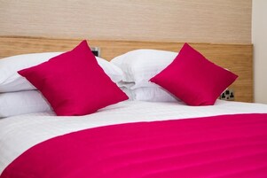 Una cama con ropa blanca y dos almohadas rojas brillantes.