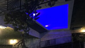 A building with a blue-lit interior space, possibly a pool or atrium, surrounded by vegetation and a metal railing. - Yaprak Dag Evi (Sapanca)