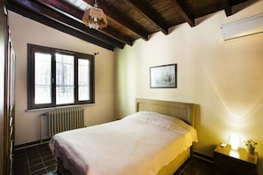 Une chambre à coucher avec un lit, une fenêtre, un radiateur, une table de chevet avec une lampe et un tableau encadré au mur.