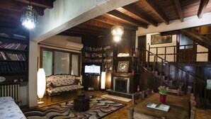 A cozy living room with a fireplace, bookshelves, a television, and a staircase. - Yaprak Dag Evi (Sapanca)