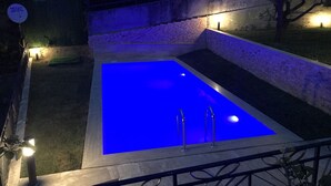A rectangular swimming pool with a blue interior, surrounded by a low stone wall, and illuminated by several ground lights. - Yaprak Dag Evi (Sapanca)
