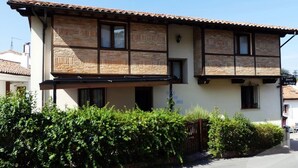 A two-story building with a tiled roof, wooden window frames, and a balcony. - Pasaje San Jorge (Comillas)