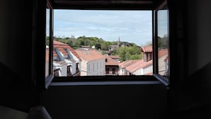 A view through an open window of a town with red-tiled rooftops and a church on a hill. - Pasaje San Jorge (Comillas)