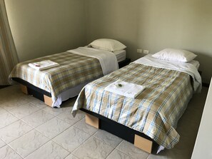 Deux lits simples avec une literie à carreaux et des oreillers blancs, des têtes de lit en bois et un sol carrelé.