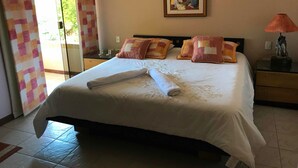 Cama bem arrumada com uma toalha enrolada, um quadro na parede e uma luminária na mesa de cabeceira.