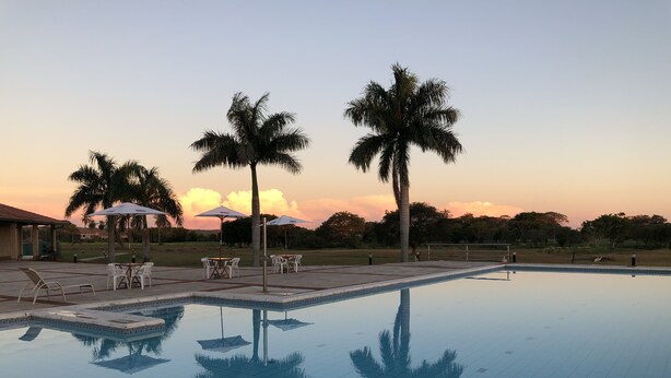 Piscina com piso em azulejos, cercada por palmeiras e mobiliário de exterior com guarda-sóis.