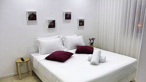 A neatly made bed with white linens and two red pillows, a small wooden stool, and a vase with flowers on the nightstand. - Nine Senses Guest House (Ovar)