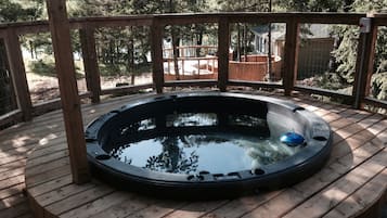 Relax in a hot tub on a raised deck with a view of the surrounding trees and wooden structure.
