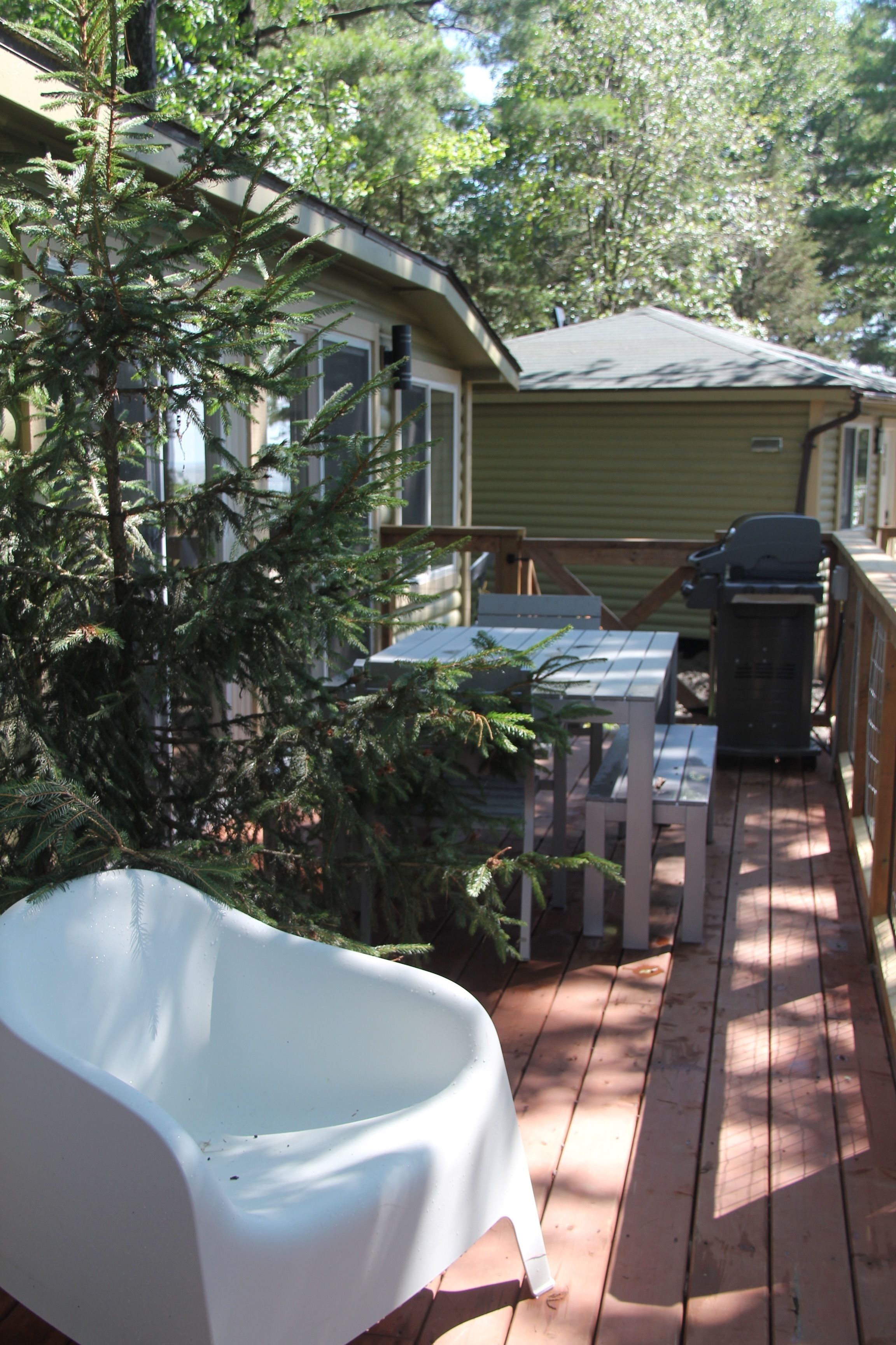 A wooden deck with a white bathtub, a table, and a grill.