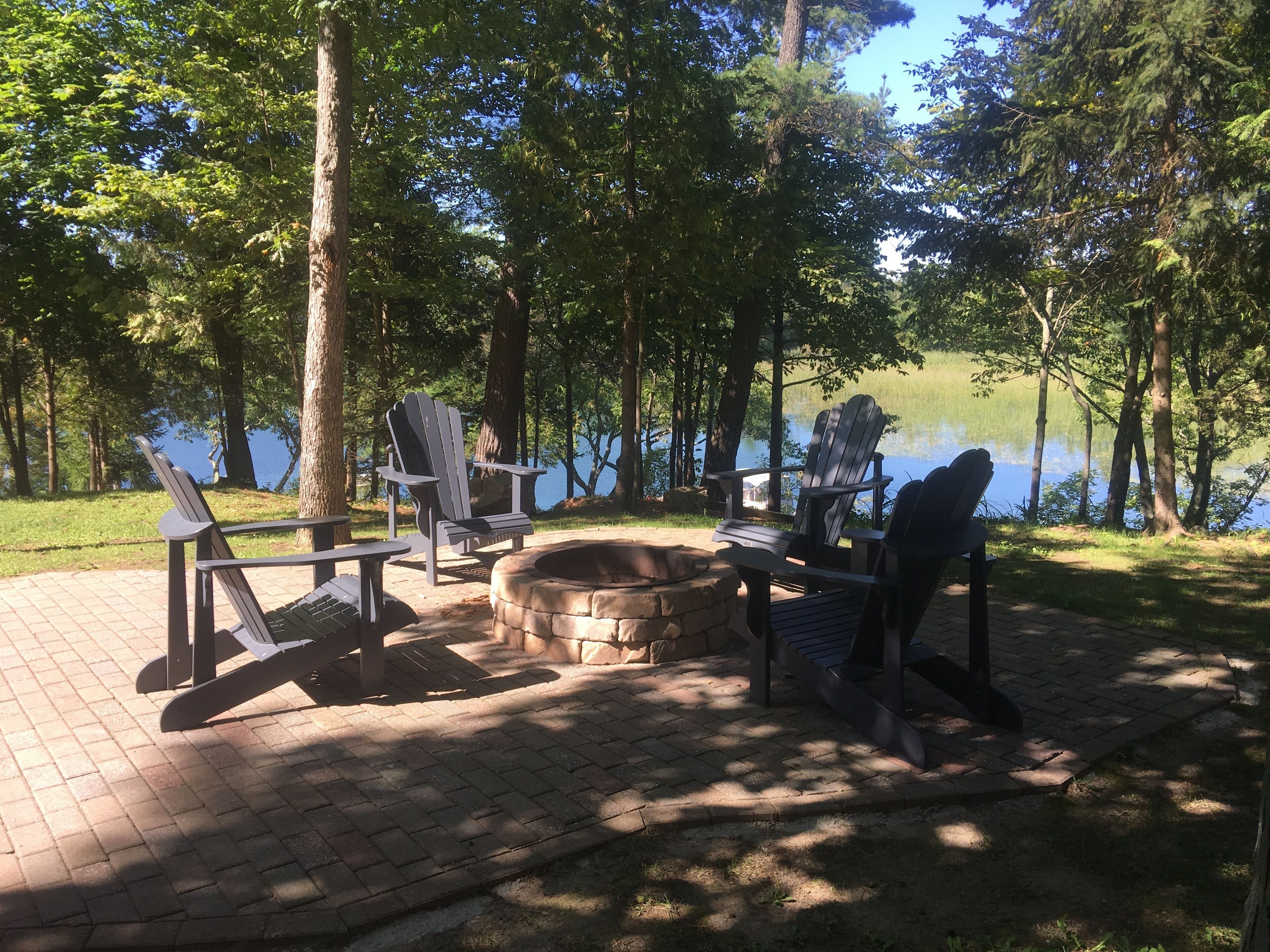 Un espace extérieur aménagé au bord du lac, avec des chaises Adirondack et un foyer en pierre.