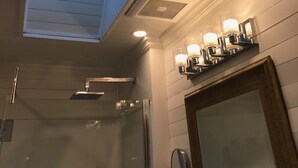 Ein Dachfenster in einem Badezimmer mit Blick auf Bäume, einer Dusche und Wandleuchten.