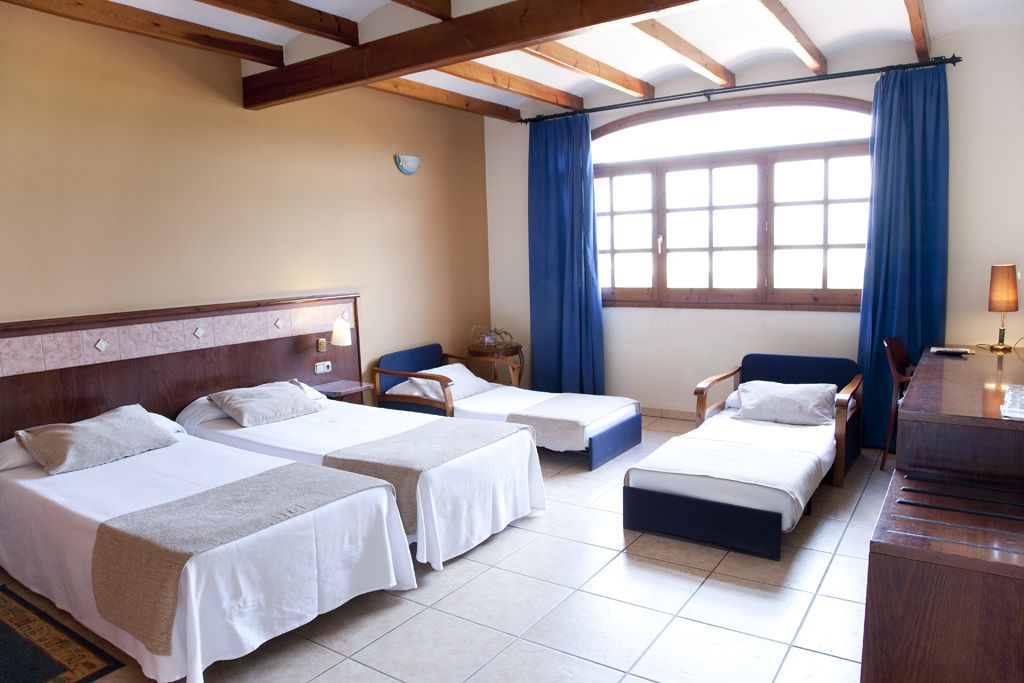 Une chambre d’hôtel avec deux lits simples, un bureau, une chaise et une fenêtre avec des rideaux.