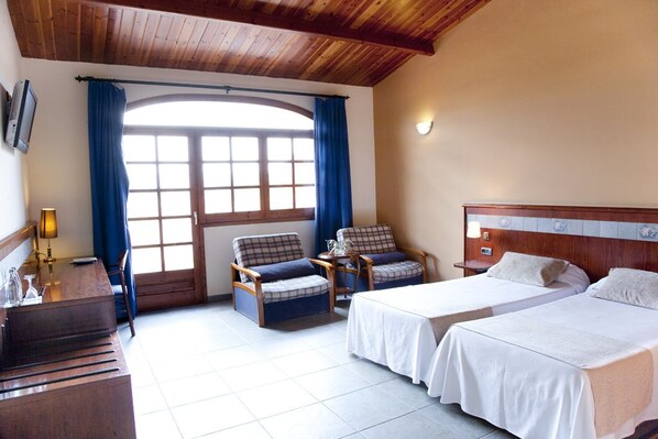 A hotel room with two beds, a wooden desk, a chair, and a large window with curtains. - Hotel Mas de la Sala (Sallent)