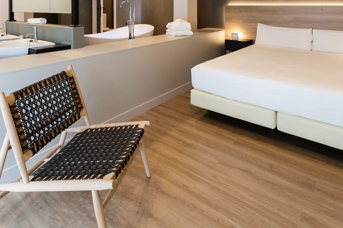 Quarto de hotel moderno com uma cama grande, área de estar com uma poltrona, toucador com espelho e banheiro com banheira.