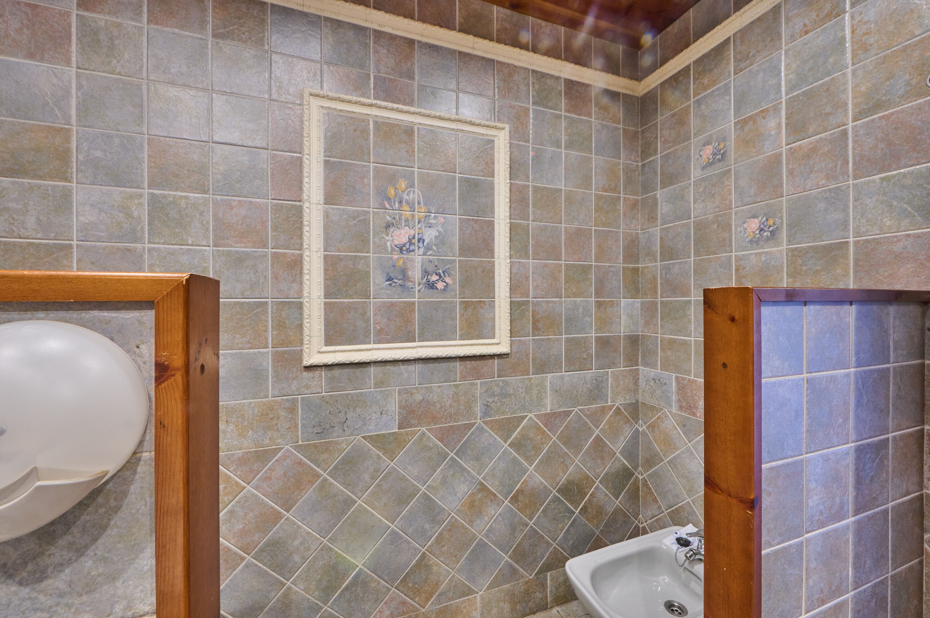 Ein Badezimmer mit gefliesten Wänden, einem gerahmten Bild, einem Waschbecken und einer Toilette.