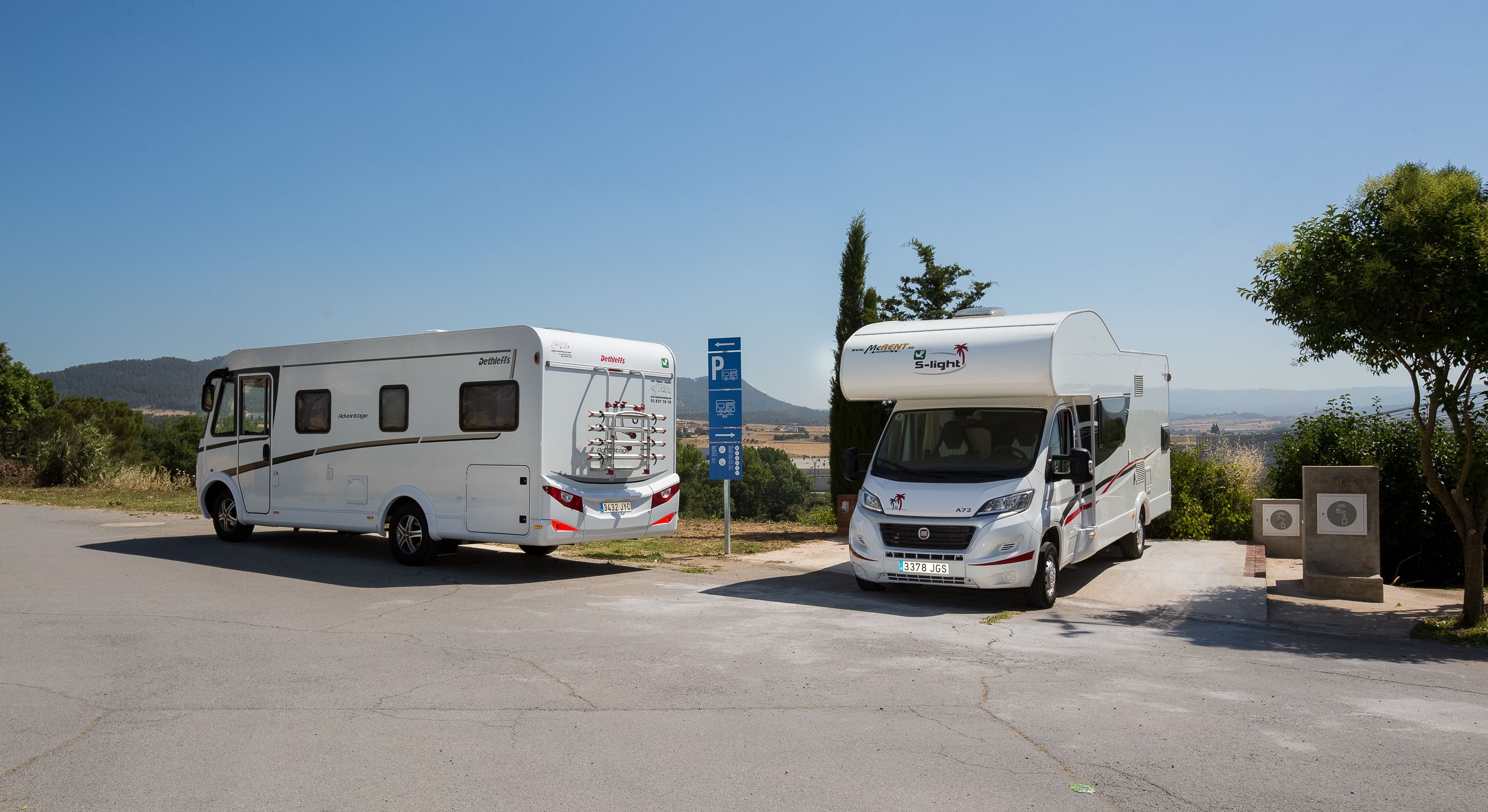 Dos vehículos recreativos estacionados en un camping con vista despejada al paisaje circundante.