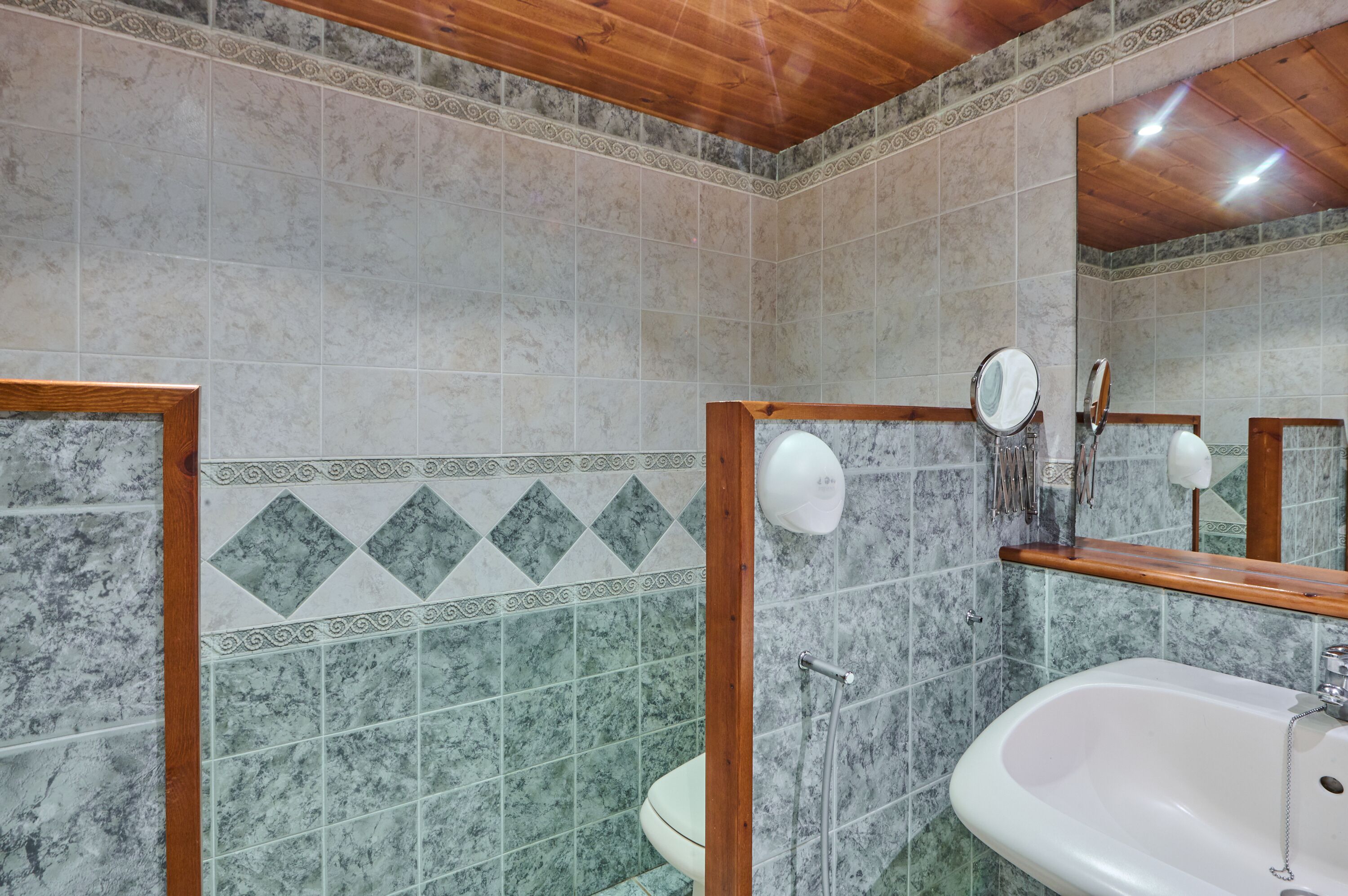 Un baño con pared de azulejos de mármol, un espejo con marco de madera, un lavamanos blanco y un inodoro.