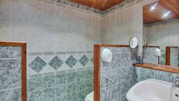 Un baño con pared de azulejos de mármol, un espejo con marco de madera, un lavamanos blanco y un inodoro.