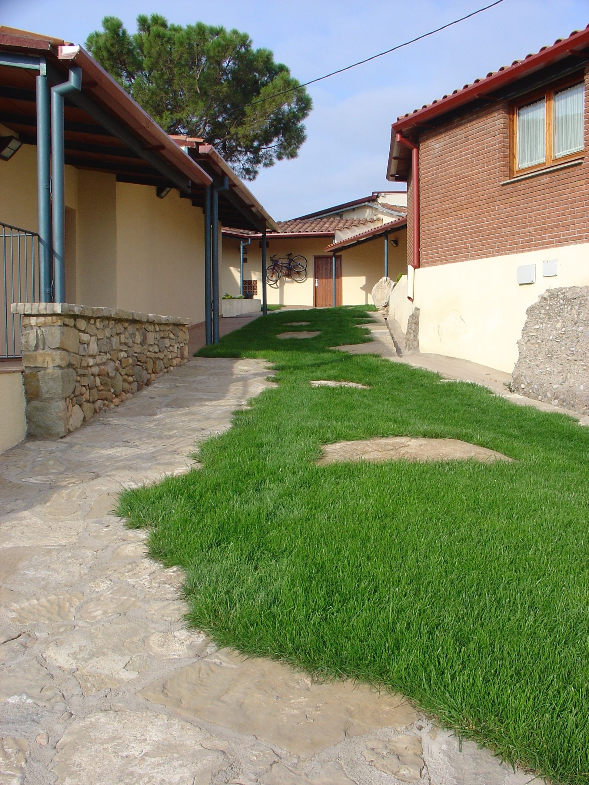 Un patio con un sendero de piedra, zona verde y un edificio con techo de tejas y paredes de ladrillo.