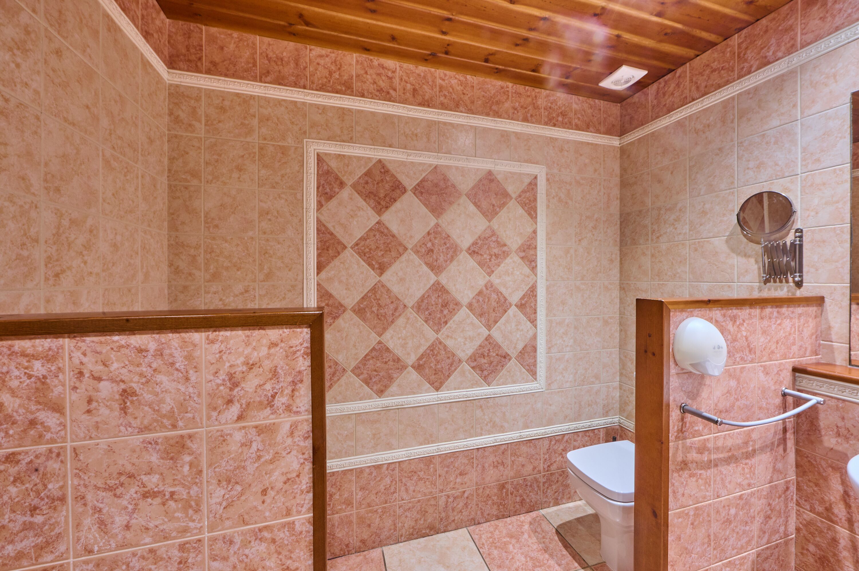 A bathroom with a wooden ceiling, a white toilet, a hand dryer, and a mirror.