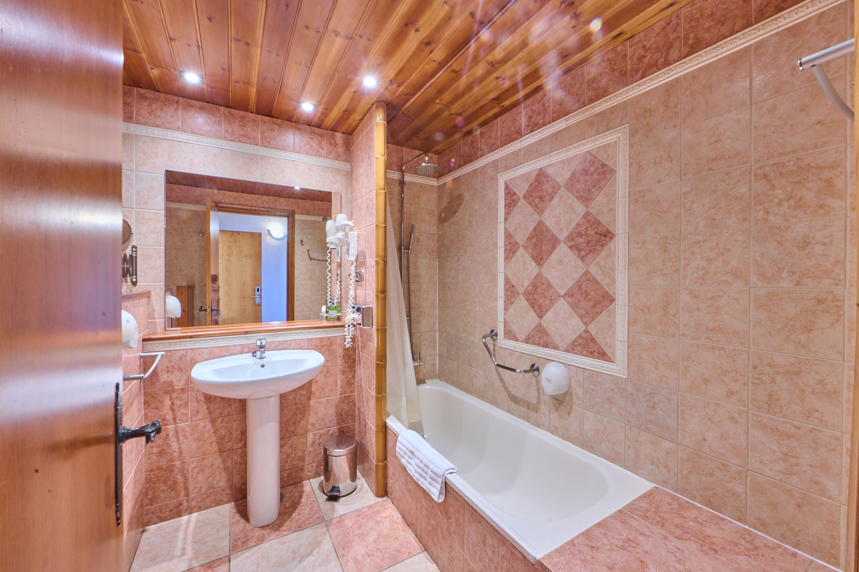A bathroom with a wooden ceiling, a sink, a bathtub, and a shower.