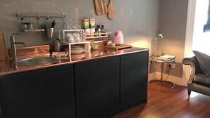 Una cocina con una isla central, un lavamanos y una encimera con varios objetos. Hay utensilios de madera colgados en la pared, una tetera y una cafetera en la isla.