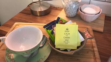 Una encimera de cocina con una taza y platillo verde, un tazón de bolsitas de té, una jarra y un tazón rosa.