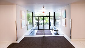 A modern hotel lobby with a carpeted floor, glass doors leading outside, and a bench along the wall. - Pelicanstay in Burnaby (Burnaby)