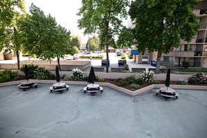 A courtyard with picnic tables and umbrellas, surrounded by trees and a parking area. - Pelicanstay in Burnaby (Burnaby)