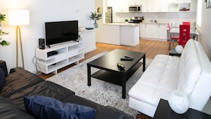 A modern living room with a flat-screen TV, a black coffee table, a white sofa, and a red chair. - Pelicanstay in Burnaby (Burnaby)