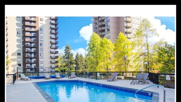 A rectangular swimming pool with a blue interior, surrounded by a concrete deck and a black metal fence. There are lounge chairs along the poolside. - Pelicanstay in Burnaby (Burnaby)