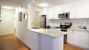 A modern kitchen with white cabinets, stainless steel appliances, and a granite countertop. - Pelicanstay in Burnaby (Burnaby)