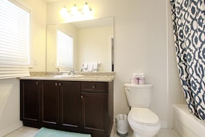 Un baño con un mueble de tocador de madera oscura, un inodoro blanco y una cortina de ducha estampada.