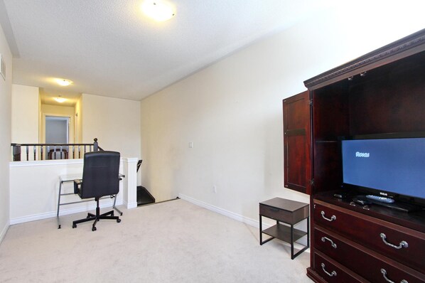 A room with a wooden cabinet, a television, a desk, and a chair.