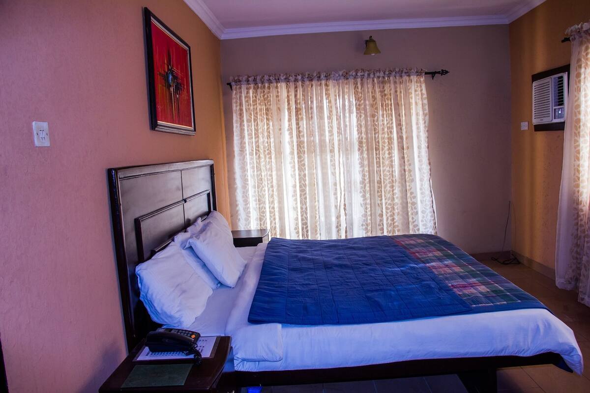 A bedroom with a bed, a nightstand, a telephone, and a painting on the wall.
