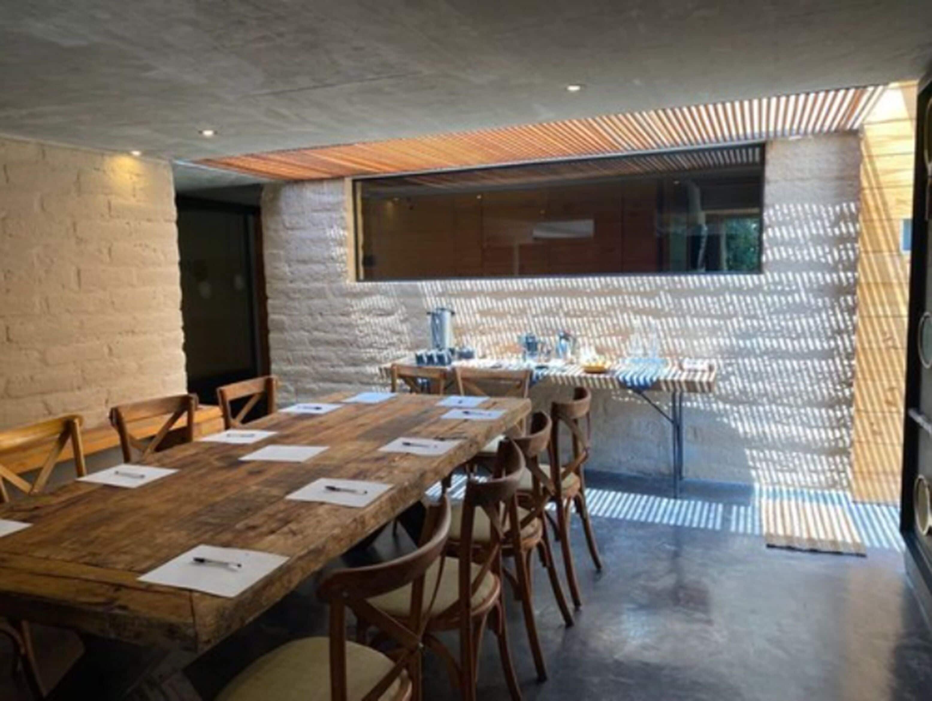A conference room with a long wooden table, several chairs, and a patterned wall.